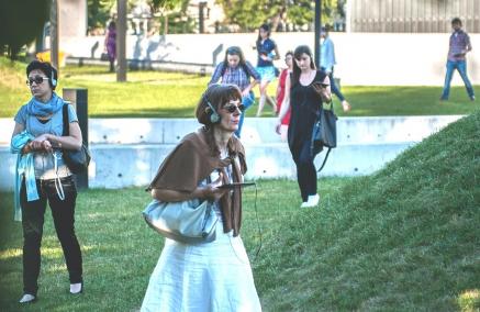 Kilka kobiet w słuchawkach spaceruje po zielonej łące przy Muzeum POLIN.