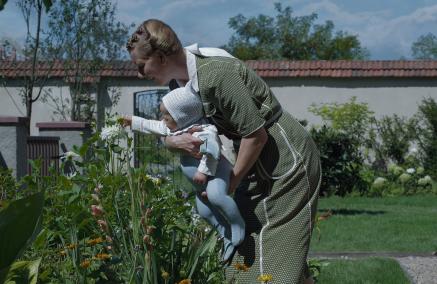 Kadr z filmu "Strefa interesów" - kobieta, prawdopodobnie żona komendanta Auschwitz, trzyma dziecko nad kwitnącymi kwiatami.