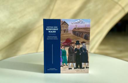 Okładka książki o Majerze Kirszenblacie stoi na tle krzywoliniowej ściany w Muzeum POLIN.
