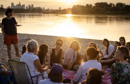 Grupa osób uczestnicząca w Muzealnym Think-tanku siedzi na plaży nad Wisłą w Warszawie.