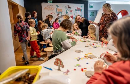 Grupa dzieci wraz z opiekunami tworzy prace plastyczne przy stole w Miejscu edukacji rodzinnej "U króla Maciusia". 