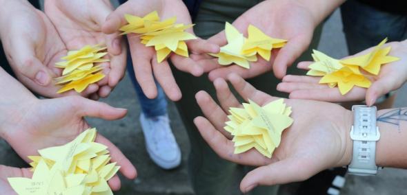 Na zdjęciu widać osiem dłoni, na których leżą żółte papierowe żonkile, symbol akcji społeczno-edukacyjnej Żonkile