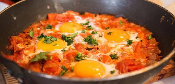 Wielka patelnia a w niej gorąca szakszuka - potrawa złożona z sosu pomidorowo-warzywnego z sadzonymi jajkami