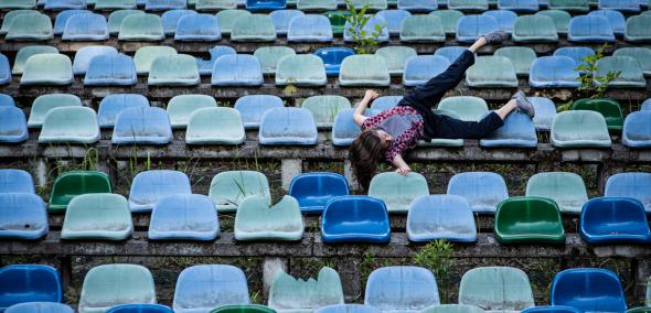 Na niebieskich stadionowych plastikowych krzesełkach leży jedna osoba, z głową w dół