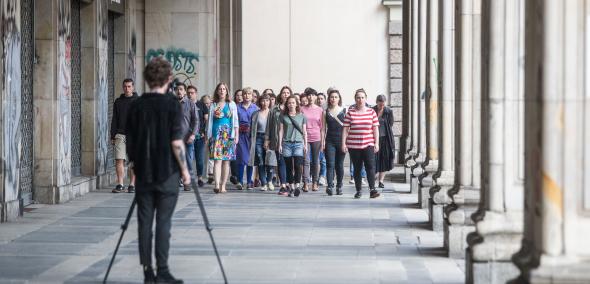 Na obrazie widzimy grupę osób - kobiet i mężczyzn w różnym wieku, przed którymi stoi fotograf.