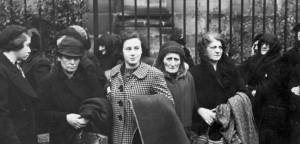 Czarno-białe zdjęcie. Grupa żydowskich kobiet stoi przed bramą.