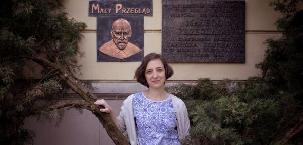 Przewodniczka Julia Chimak na tle tablicy upamiętniającej Janusza Korczaka.