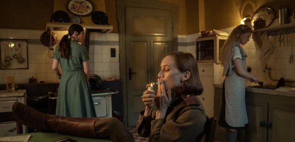 Kadr z filmu "Pociąg donikąd". W pomieszczeniu są trzy kobiety - dwie stoją, jedna siedzi z nogami założonymi na stole i pali papierosa.