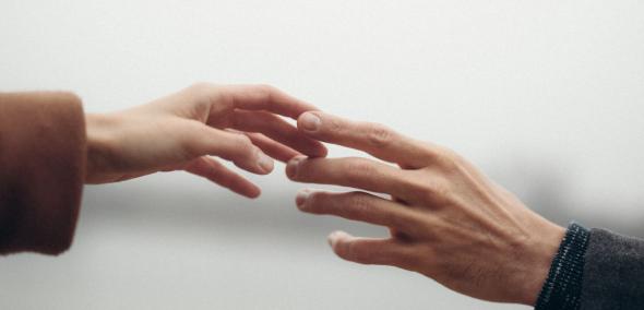 Dwie osoby wyciągają ku sobie dłonie i dotykają się opuszkami palców.