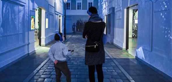 Kobieta z dzieckiem w słuchawkach w galerii "Na żydowskiej ulicy" na wystawie stałej w Muzeum POLIN.