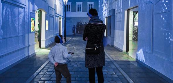 Kobieta z dzieckiem w słuchawkach w galerii "Na żydowskiej ulicy" na wystawie stałej w Muzeum POLIN.
