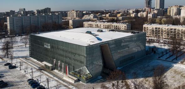 Budynek Muzeum POLIN z zewnątrz, pokazany z góry, z drona. W tle bloki i biurowce.