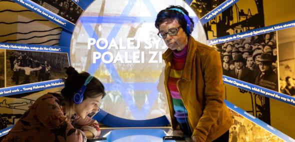 Dwie kobiety ze słuchawkami na uszach zwiedzają wystawę stałą w Muzeum POLIN.