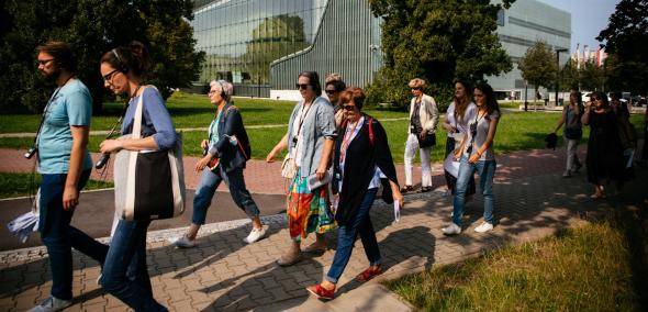 Uczestnicy spaceru z przewodnikiem idą ulicą ulicą Anielewicza. W tle drzewa i budynek Muzeum POLIN.