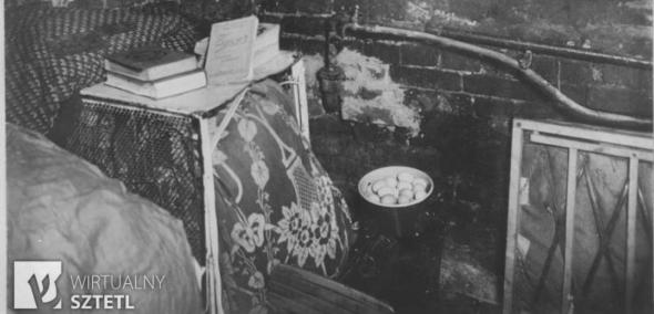 Wnętrze kryjówki w getcie warszawskim w czasie powstania 1943 roku. Na stoliku leżą książki, w wiaderku poniżej - jajka. Wokół miniaturowe meble. 