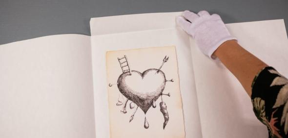 Konserwator zbiorów trzyma przed sobą rysunek serca przebitego strzałami i drabiną.