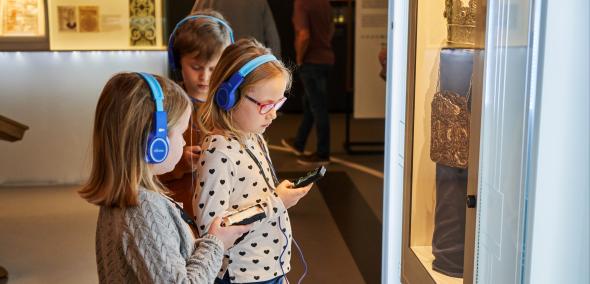 Dzieci z audioprzewodnikami zwiedzają wystawę muzeum 
