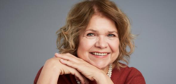 Anna Bikont - uśmiecha się i opiera obie dłonie na brodzie.
