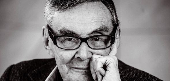 Marian Turski opiera dłoń o brodę. Zdjęcie czarno-białe.