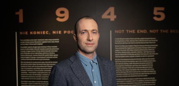 Kamil Kijek na tle planszy z tytułem wystawy "1945. Nie koniec, nie początek".