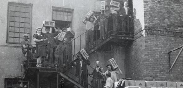 Supplies being taken off a horse-drawn wagon and being carried into a warehouse in Warsaw; the crates are labeled "JOINT".