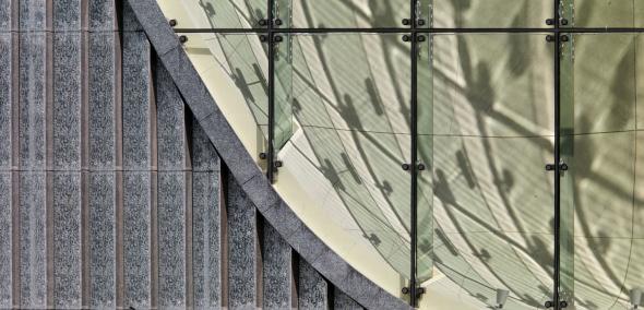 Widoczny fragment elewacji budynku, ozdobiony szklanymi panelami i fragment okna, z widoczną za nim ścianą z piaskowca