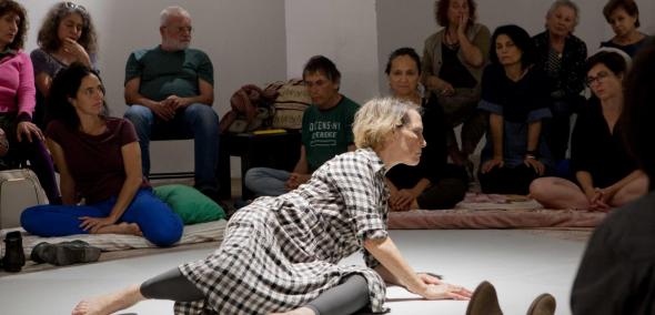 In between - performans Adiny Bar-On w Muzeum POLIN, Na zdjęciu: grupa kobiet i mężczyzn siedzi na podłodze pod ścianami pomieszczenia, na środku podłogi kobieta (Adina Bar-On) w trakcie performansu.