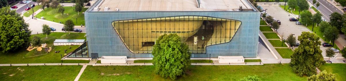 Budynek Muzeum POLIN w otoczeniu drzew, zieleni, bloków na Muranowie i wieżowców Intraco przy Dworcu Gdańskim.
