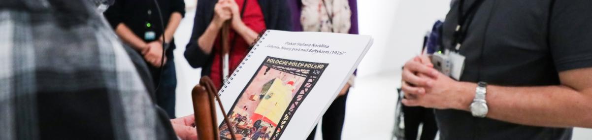 Mężczyzna trzyma w dłoniach tyflografikę. Obok niego stoi przewodnik i pozostała część grupy.