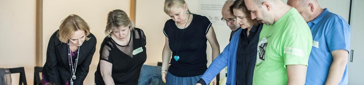 Grupa ludzi patrzy na leżące na podłodze kartki papieru.