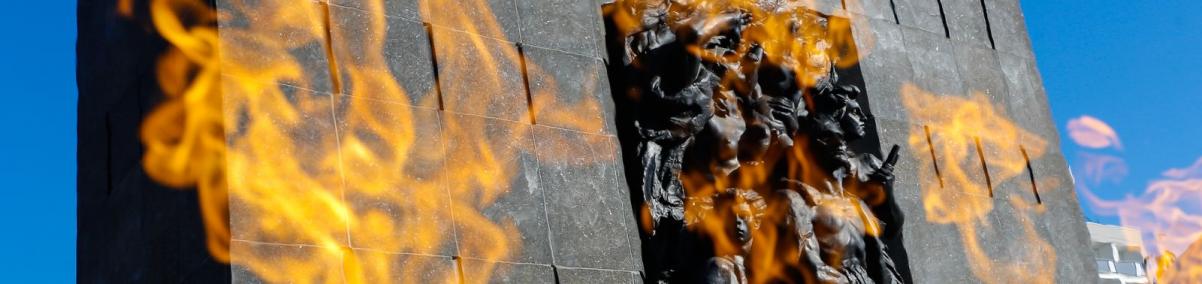 Pomnik Bohaterów Getta - duży monument z granitu z rzeźbionymi postaciami Żydów z getta warszawskiego, widziany zza płomieni palących się przed nim zniczy