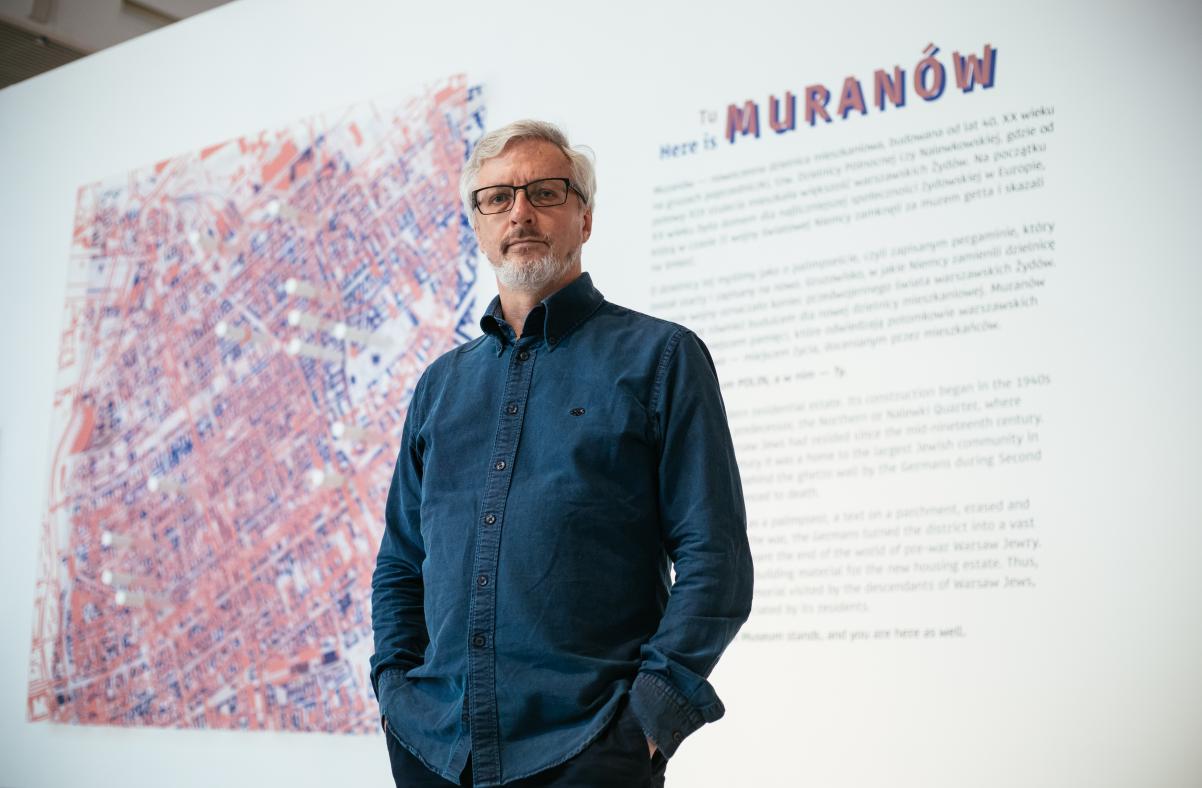 Przed planszą któa otwiera wystawę Tu Muranów stoi mężczyzna - Jacek Leociak. Na planszy opis wystawy oraz mapa Muranowa