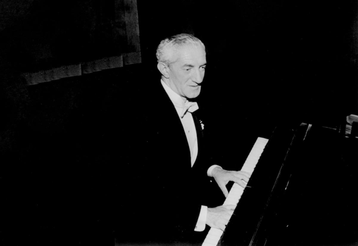 Czarno-białe zdjęcie przedstawia Henryka Warsa przy fortepianie. Ubrany jest w czarny frak i białą koszulę.