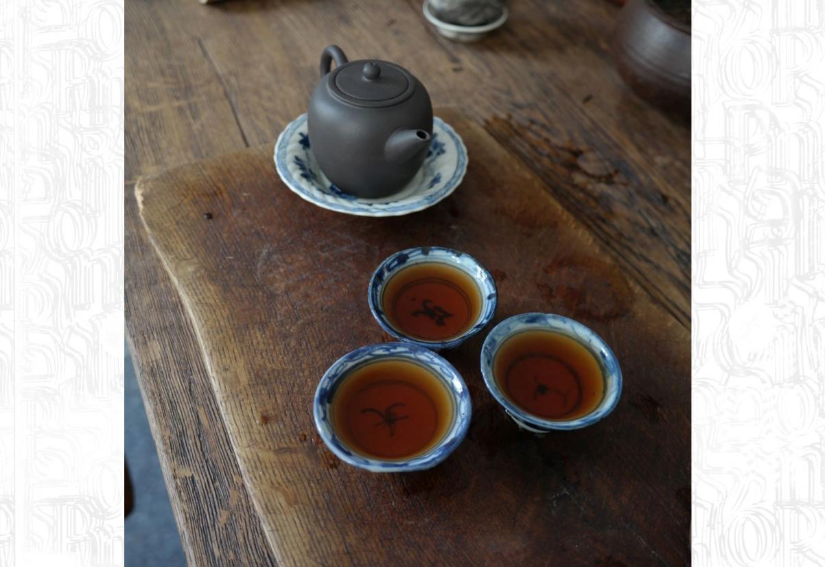Na ciemnej desce ze starego drewna stoi czajniczek i czarki z herbatą