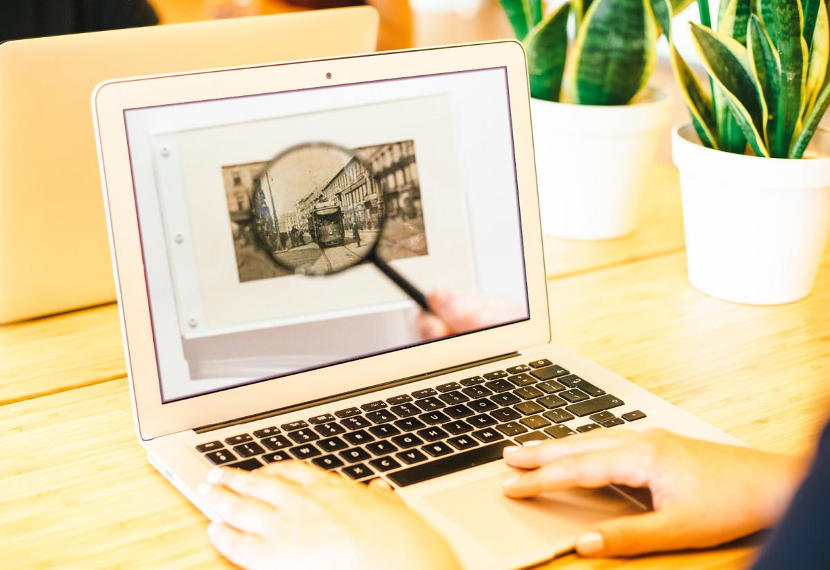 Ekran laptopa. Na nim wyświetlona jest grafika, na której znajduje się stara fotografia pod lupą.
