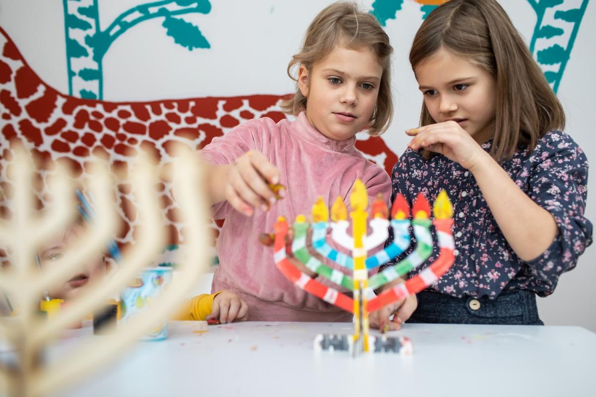 Dwie dziewczynki przyglądają się kolorowemu świecznikowi, mają uniesione dłonie, tak jakby chciały go dotknąć.