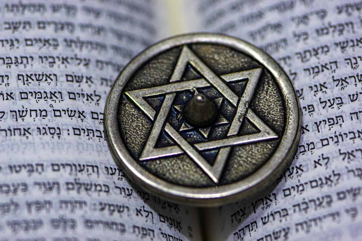 Na księdze w języku hebrajskim leży mały okrągły stalowy przedmiot z wyrytą na środku gwiazdą Dawida.