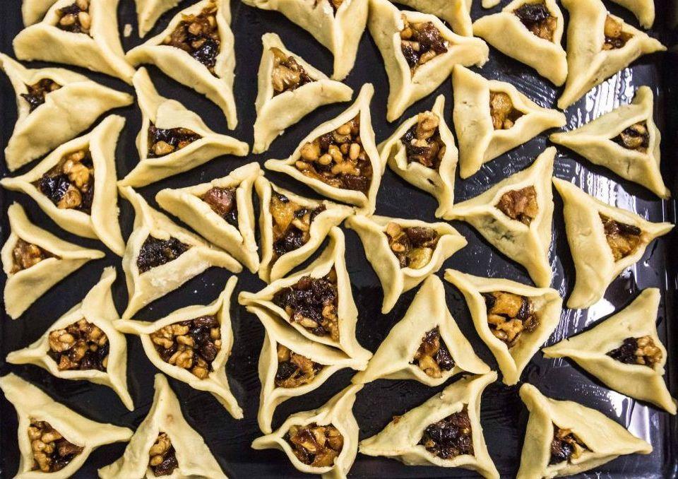 na czarnej blasze do pieczenia leżą hamantasze - tradycyjne żydowskie ciasteczka wypiekane na Purim - trójkątne, wypełnione konfiturą i orzechami