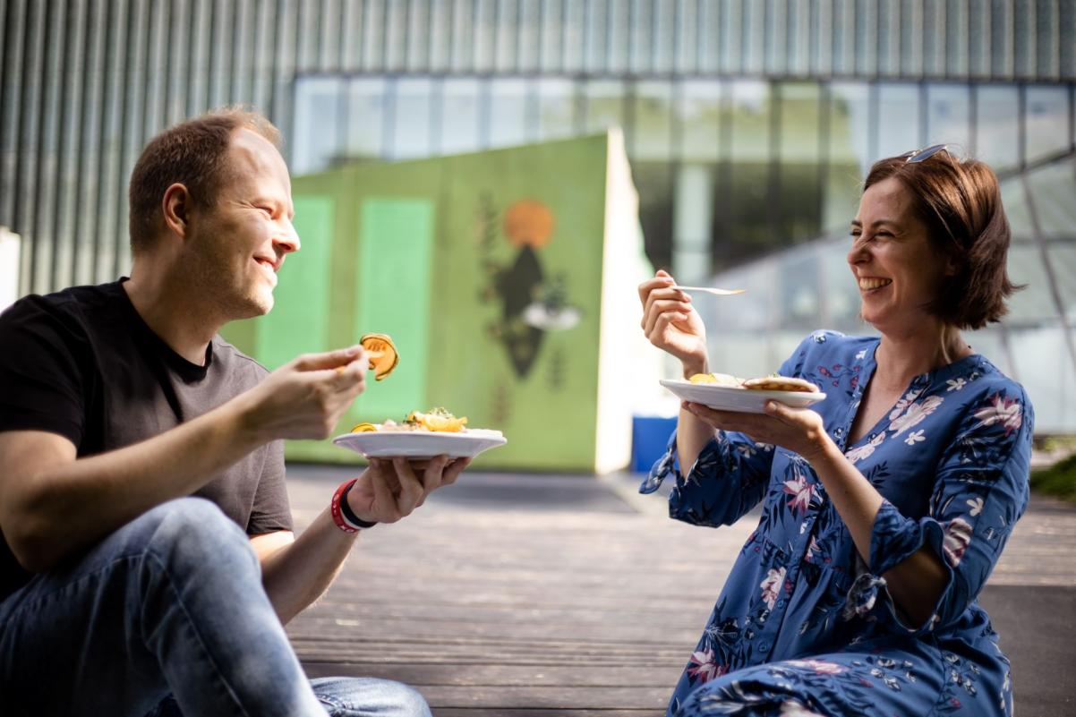Kobieta i mężczyzna trzymają talerze z jedzeniem. Śmieją się do siebie.