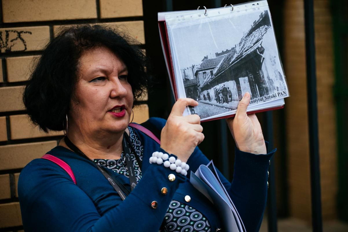 Przewodniczka Katarzyna Jakubowicz prezentuje archiwalne zdjęcie podczas spaceru miejskiego.