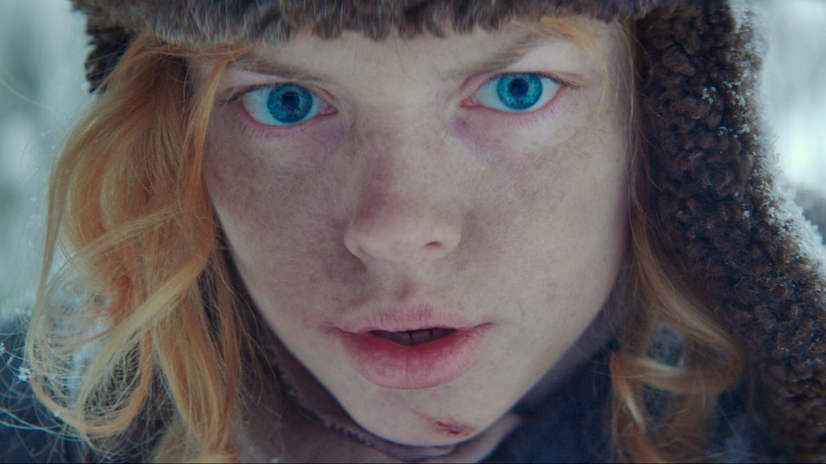 Kadr z filmu Berenshtein. Rudowłosa niebieskooka osoba w czapce.