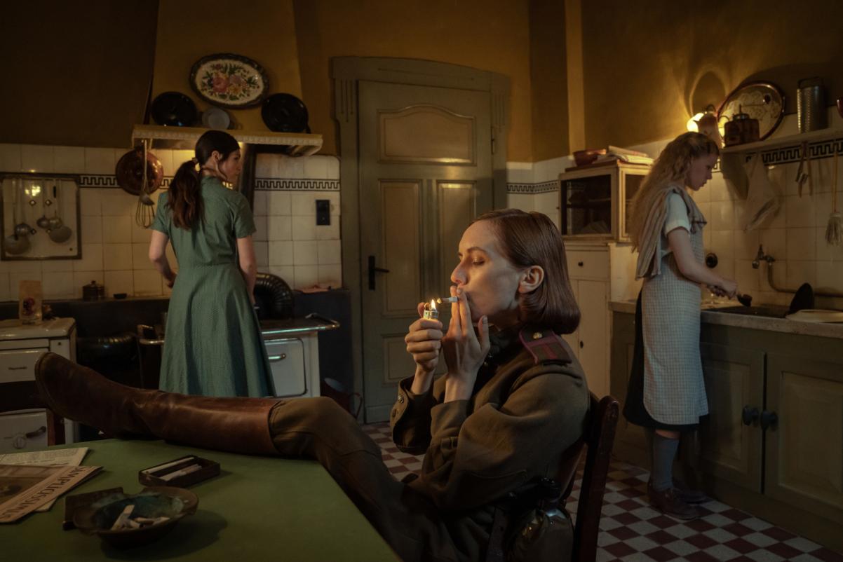 Kadr z filmu "Pociąg donikąd". W pomieszczeniu są trzy kobiety - dwie stoją, jedna siedzi z nogami założonymi na stole i pali papierosa.