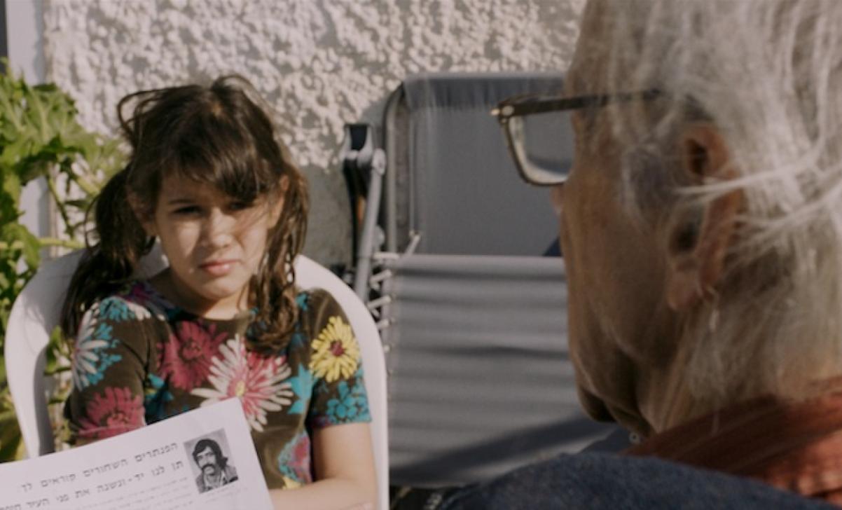 Kadr z filmu "Odrzuceni w Ziemi Obiecanej". Naprzeciwko siebie siedzą starszy mężczyzna i młoda kobieta. 