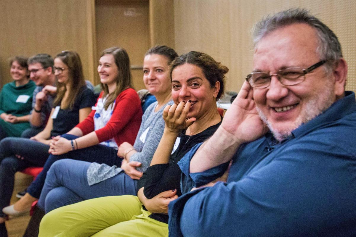Grupa uśmiechniętych osób siedzi w rzędzie w sali konferencyjnej w Muzeum POLIN.