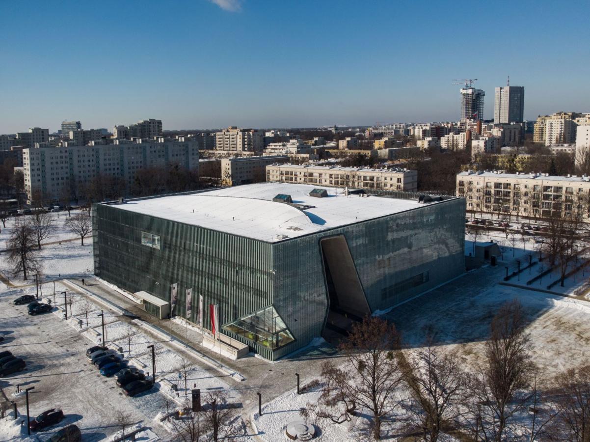 Budynek Muzeum POLIN z zewnątrz, pokazany z góry, z drona. W tle bloki i biurowce.