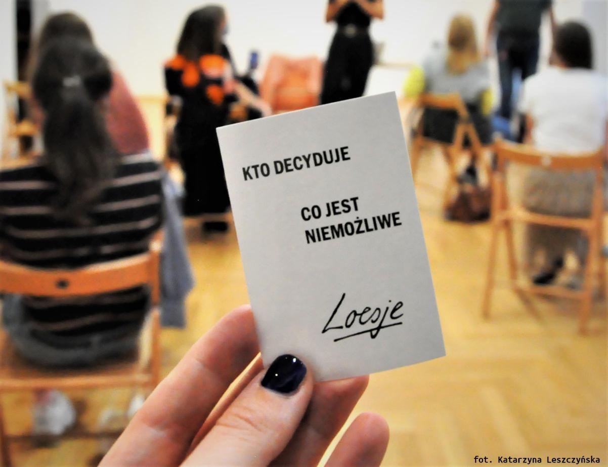 Kobieta trzyma przed sobą kartkę z napisem Kto decyduje, co jest niemożliwe. Loesje.