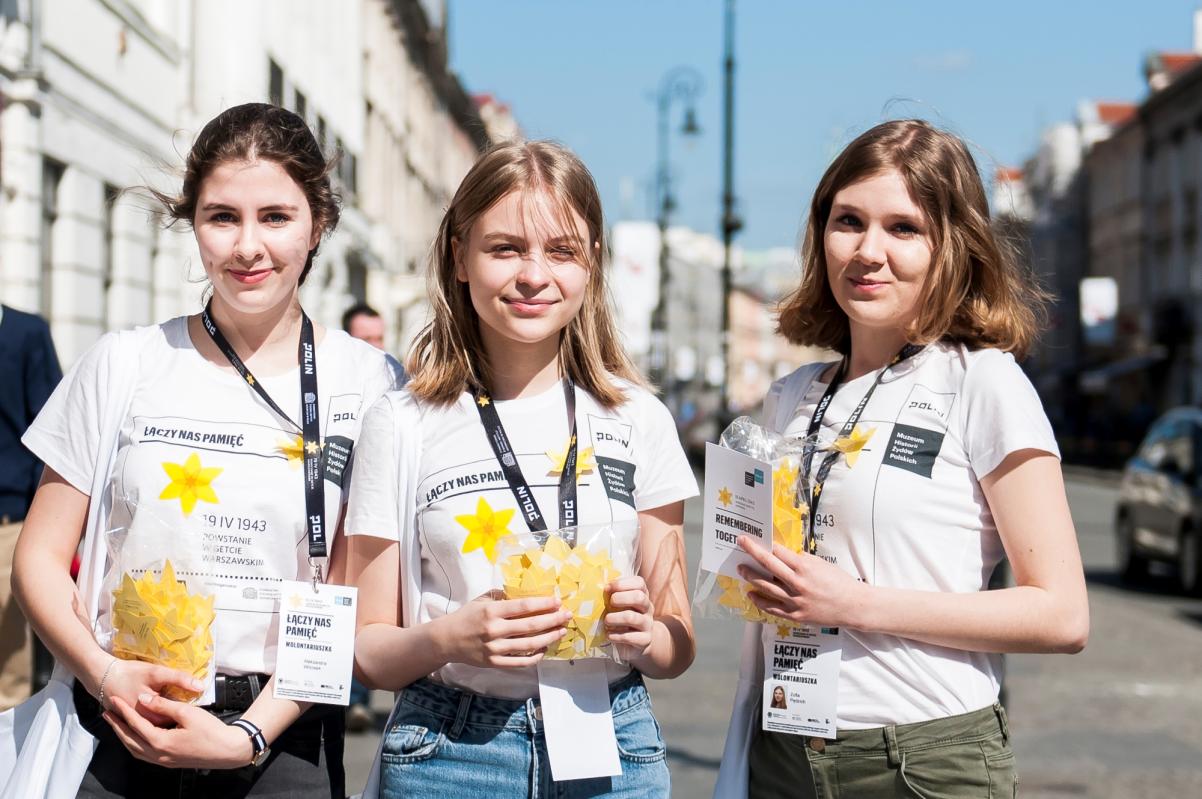 Trzy uśmiechnięte wolontariuszki akcji Żonkile trzymają torby foliowe pełne papierowych żonkili.