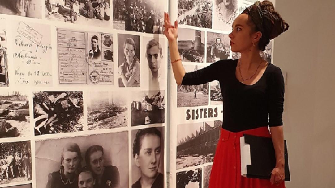 Zuzanna Hertzberg wskazuje dłonią zdjęcie na planszy na wystawie "Bojowniczki. Archiwum afektywne".
