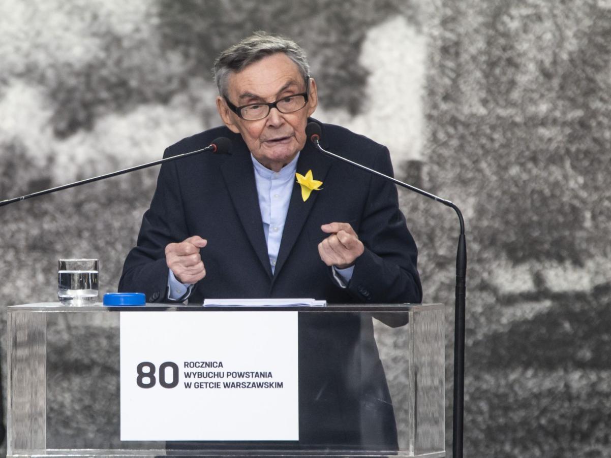 Marian Turski wygłasza przemówienie podczas obchodów 80. rocznicy powstania w getcie warszawskim. Stoi przy pulpicie mównicy, na której naklejona jest tabliczka z napisem "80 rocznica powstania w getcie warszawskim""