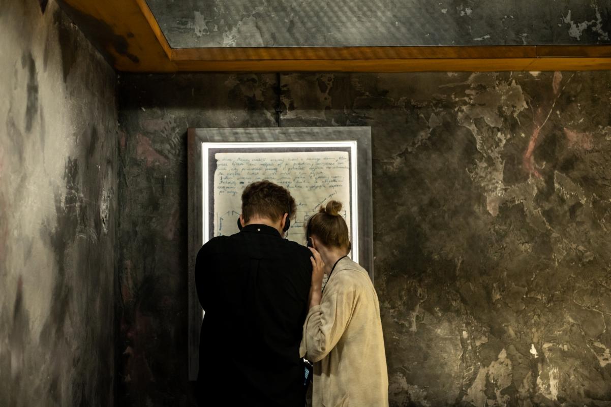 Przestrzeń wystawy "Wokół nas morze ognia". Kobieta i mężczyzna oglądają zapiski osób ukrywających się w bunkrach podczas powstania w getcie warszawskim.